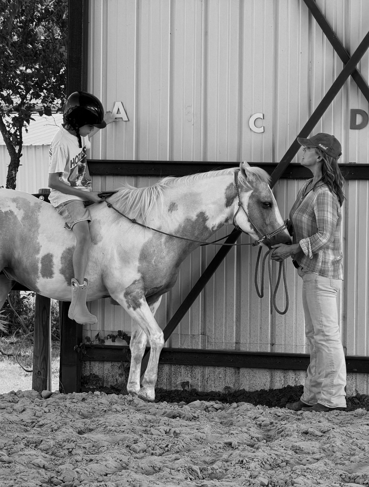 Nicol Ragland helps a young client experience equine therapy on horseback, black and white print.